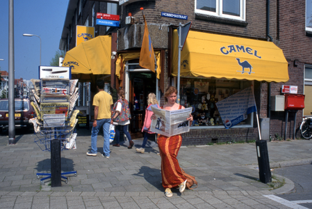 846315 Afbeelding van een jonge vrouw die de krant Het Utrechts Nieuws leest bij sigarenmagazijn De Post (Jan van ...
